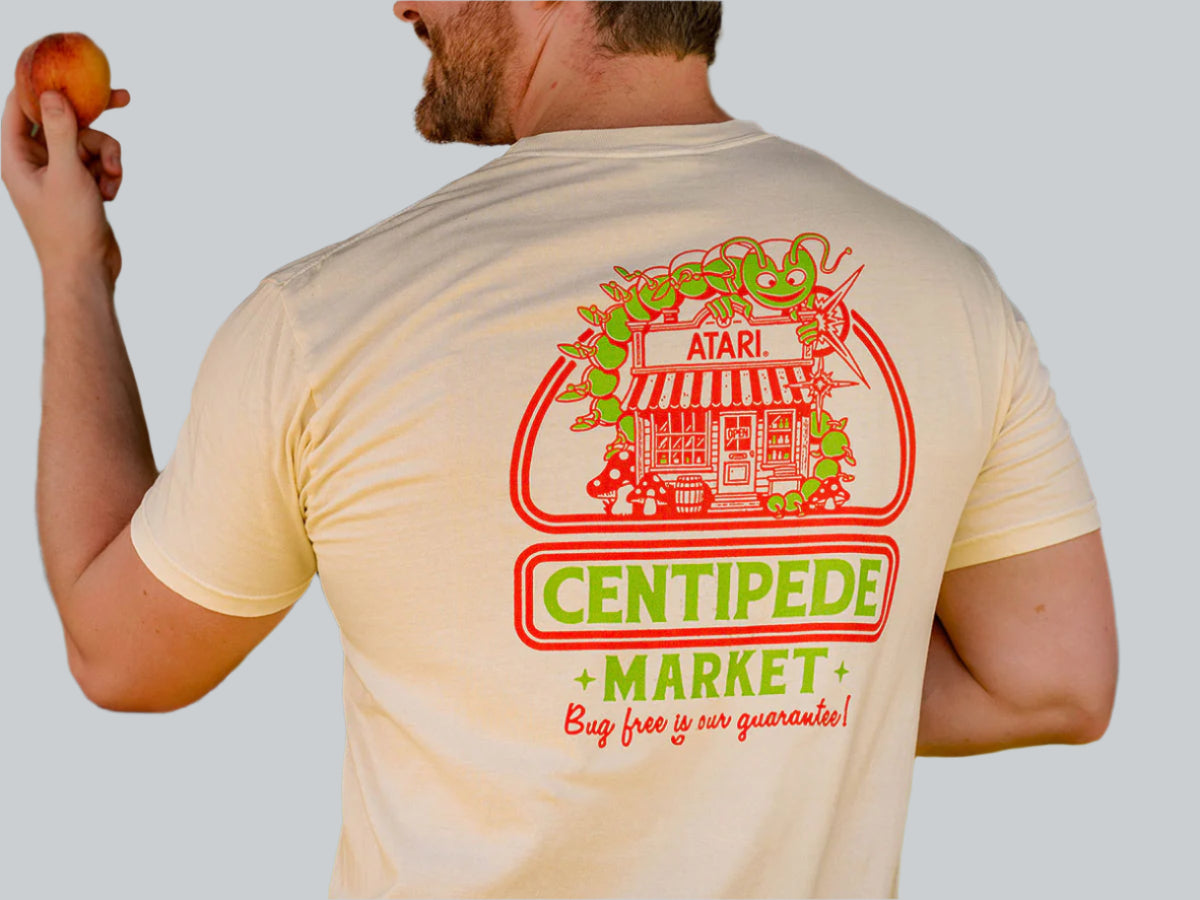 Person wearing a t-shirt with a Centipede Market graphic on the back, holding an apple.